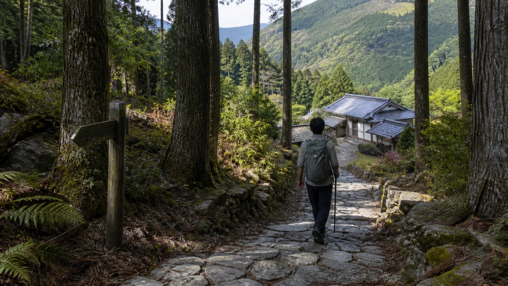 Walker on the stone-paved Kumano Kodo Nakahechi trail approaching a small mountain inn in cedar forest